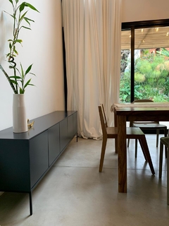 Vista lateral izquierda del mueble consola color gris, que tiene cinco puertas y cuatro patas metálicas, ambientado en un living.