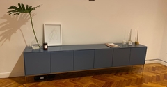 Vista de frente del mueble consola, color azul, que tiene seis puertas y cinco patas metálicas al piso.