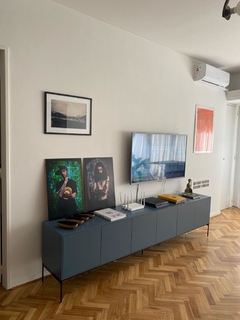 Vista de frente con inclinación hacia la derecha del mueble consola color azul, con seis puertas y cinco patas metálicas al piso, ambientado en un living.