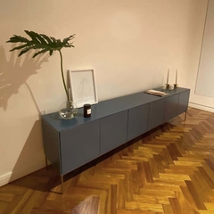 Vista a 45° hacia la derecha del mueble consola, que tiene seis puertas y cinco patas metálicas al piso.