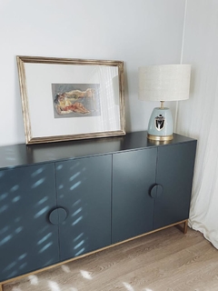 Vista de frente del mueble Vajillero color azul, que tiene cuatro puertas con tiradores decorados, y cuatro patas metálicas, ambientado en un living.