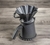 Vista de perfil com valorização do pegador de um Kit de Jarra e Coador de Café V60-02 em Cerâmica com esmaltação branca da Felline Cerâmica. O Coador está encaixado na jarra, ao lado tem um pequeno corta pingos também na cor branca. O conjunto está sobre 