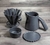 Kit de Jarra e Coador de Café 102 em Cerâmica com esmaltação preta da Felline Cerâmica. Vista de 4 peças deste conjunto sobre uma mesa de madeira, coador, jarra, prato de apoio e corta pingos. 
