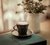 café espresso com desenho de flor em xícara e pires cor preta em cerâmica na mesa perto de janela com cortina