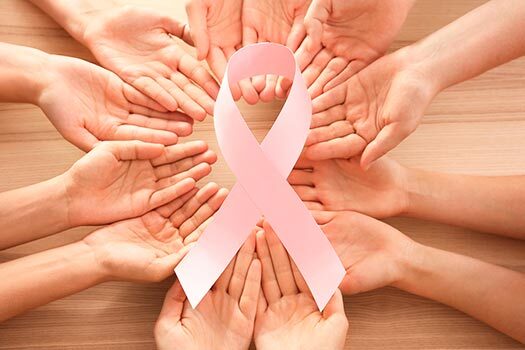Imagem de laço rosa símbolo do câncer de mama segurado por mãos femininas.