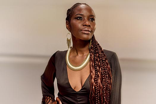 Imagem de mulher negra com cabelos trançados, usando uma blusa preta decotada e um colar dourado