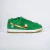 O tênis Nike Dunk Low SB St. Patrick's Day é um modelo masculino com um visual marcante, sendo predominantemente verde com detalhes em dourado no swoosh. O material é uma combinação de camurça e tecido, e o tipo de ajuste é por cadarços. Este modelo está 