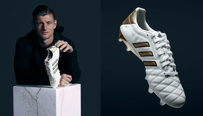 Chuteira Adidas 11PRO TK FG Toni Kroos Branca e Dourada em edição limitada. O cabedal de couro premium apresenta detalhes dourados, enquanto a sola Copa Pure para superfícies firmes ostenta a assinatura do maestro do meio-campo.