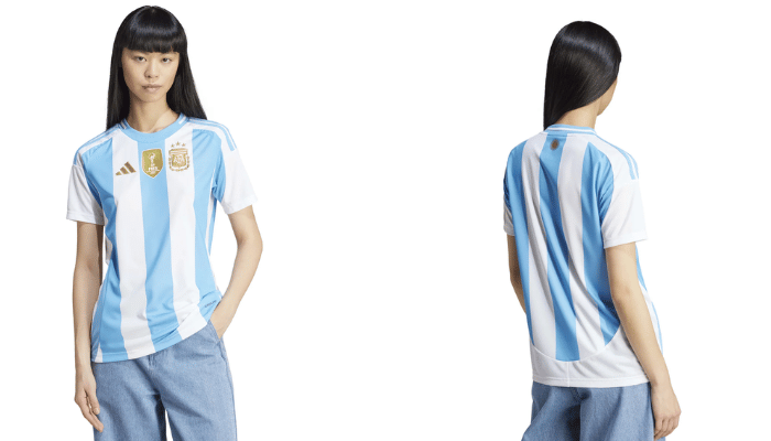 Camisa titular feminina da Seleção Argentina Adidas 2024-2025. A camisa é branca com três listras verticais azul celeste, gola redonda com faixa branca e Sol de Mayo, logos da Adidas e AFA em dourado. A modelo está vestindo a camisa e sorrindo.