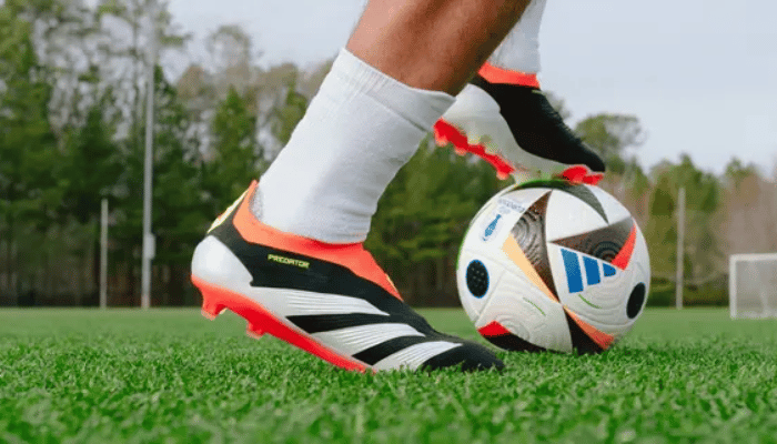 Chuteira Adidas Predator 24 Laceless FG Solar Energy em preto, branco, amarelo e vermelho. A chuteira apresenta um design moderno com detalhes em preto e branco, com as icônicas listras vermelhas da Adidas na lateral. A parte superior da chuteira é feita de um material sintético leve e respirável, com textura para melhor controle da bola.