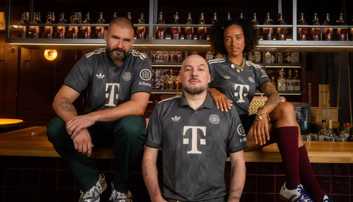 Camisa do Bayern de Munique para a Oktoberfest 2024. A peça apresenta um design inspirado no Trachten, com base cinza, padrão de diamantes, gola polo e detalhes em verde e off-white.