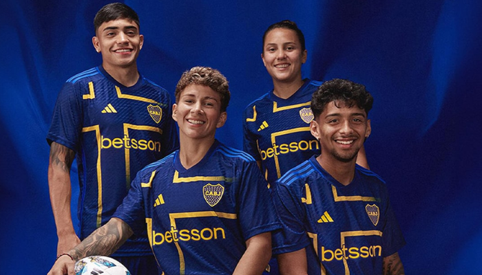  nova camisa III do Boca Juniors para a temporada 2024-2025. A camisa, predominantemente azul marinho, possui um design inspirado na história do clube, com o contorno de uma cruz amarela no peito em referência à bandeira sueca. As três listras da Adidas em azul royal, o escudo do Boca Juniors e um símbolo alternativo na nuca completam o visual.