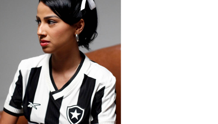 Camisa feminina titular do Botafogo 2024/2025. Listrada em preto e branco, textura de tricô, gola V branca com detalhes pretos, escudo em TPU no peito esquerdo e logo Reebok em branco no direito.