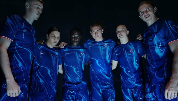 camisa titular do Chelsea FC para a temporada 2024/2025, produzida pela Nike. A camisa é predominantemente azul royal, com um design inovador que apresenta um padrão de ondas em tons mais claros da cor, simbolizando as chamas azuis. A gola é redonda e azul, enquanto os punhos combinam branco e laranja. 