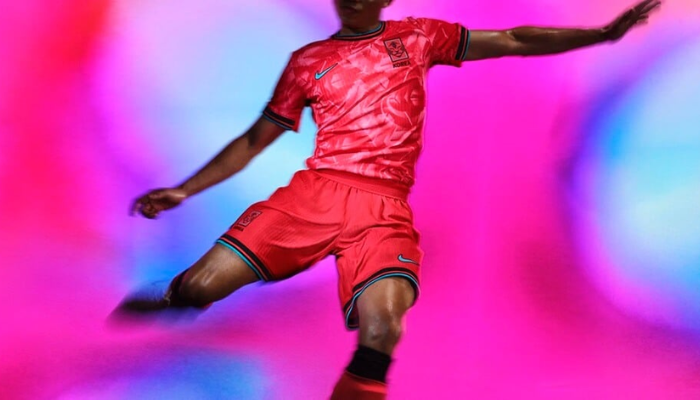 Camisa titular da Seleção Coreana Nike 2024-2025, com design inovador em rosa, preto e azul celeste. A gola redonda possui efeito de marca de garra do tigre, enquanto o escudo KFA preto vazado e o Swoosh Nike azul celeste destacam a identidade visual moderna e tradicional.