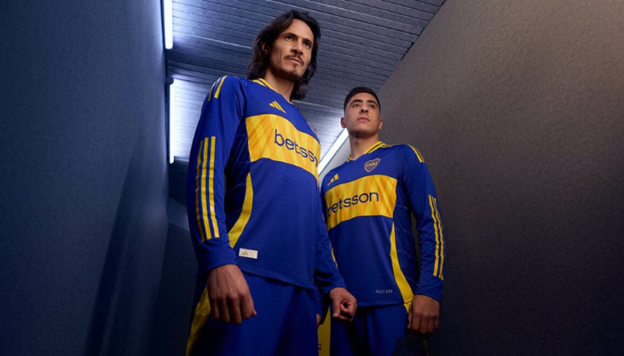 nova camisa titular do Boca Juniors para a temporada 2024-2025. O manto azul destaca a faixa dourada na barriga, inspirada no trem da La Bombonera. O logo da Adidas, o escudo do Boca e o patrocínio da Betsson completam o design, que celebra a paixão xeneize.