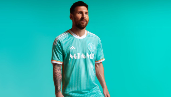 A terceira camisa do Inter Miami Adidas 2024 apresenta um design vibrante em azul celeste com linhas verticais, gola redonda branca e detalhes em laranja. O escudo do clube e o antigo logo da MLS em branco completam o visual inspirado nos anos 80, trazendo um toque nostálgico e moderno ao mesmo tempo.