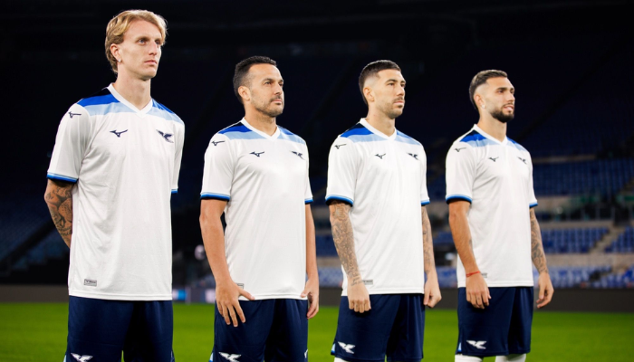 Camisa Lazio 125 Anos Mizuno 2025, modelo comemorativo branco com jacquard em chevrons. Gola V branca, faixas retrô nos ombros e punhos em três tons de azul. Escudo clássico com águia em azul marinho, logo da Mizuno na mesma tonalidade. Inscrição "9 gennaio 1900" na nuca, celebrando a fundação da Lazio.