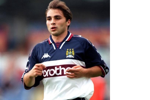 Camisa Reserva Retrô do Manchester City Kappa 1997/98, predominantemente branca com detalhes azuis e vermelhos. Logotipo da Kappa e patrocinador Brother em branco. Celebre a promoção épica para a Premier League em 1999.
