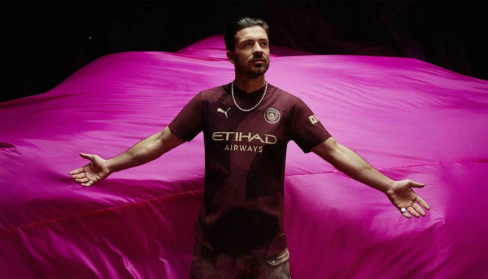 A terceira camisa do Manchester City 2024-2025 apresenta um design moderno e elegante, com as cores bordô e dourado dominando. O icônico navio do clube, presente no escudo, é destaque na parte frontal da camisa. A gola V em bordô e os detalhes dourados completam o visual