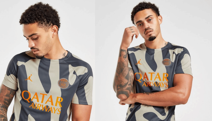 Camisa bege com logotipos laranja do PSG e da Jordan na frente. Padrão animal preto nas mangas e laterais. Modelo masculino vestindo a camisa em pé, com as mãos nos bolsos.