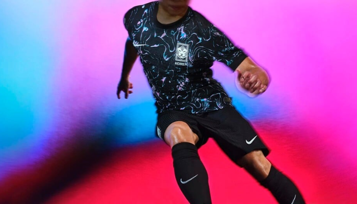 Camisa reserva da Seleção Coreana Nike 2024-2025, predominantemente preta, com grafismo em tons de rosa e azul celeste inspirado nas peças lacadas em pérola da Coreia do Sul. Possui gola redonda e punhos pretos, com o Swoosh da Nike branco no lado direito do peito e o escudo da KFA no lado esquerdo.