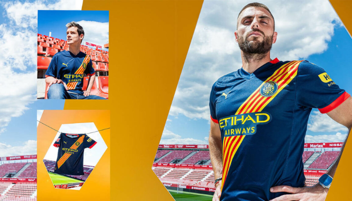 Camisa reserva do Girona FC 2024/2025: azul marinho com faixa diagonal em amarelo e vermelho, inspirada na bandeira da Catalunha. Destaques incluem o escudo do clube, logo PUMA e patrocínio Etihad.