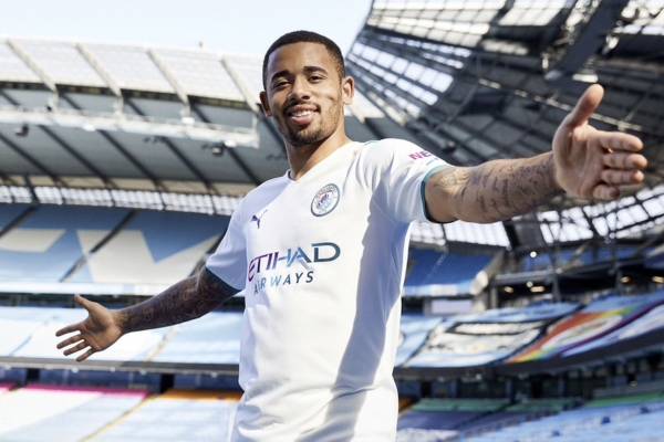 Camisa Reserva Manchester City Puma 2021-22 em elegante design branco e azul, distintivos iridescentes e patrocinadores, representando o compromisso da Cityzens Giving Foundation com água potável global.