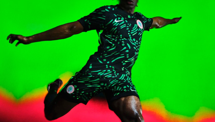 Camisa reserva da Seleção Nigeriana Nike 2024/25. A camisa é predominantemente verde-escuro com um padrão gráfico verde-limão por toda a extensão. O escudo da Seleção Nigeriana está no lado esquerdo do peito e o Swoosh da Nike está no lado direito em branco. As mangas e as laterais da camisa são verde-limão.