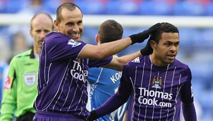Camisa reserva retrô do Manchester City da temporada 2007-2008. A camisa apresenta um design listrado roxo e branco, o escudo do clube no peito e o patrocinador Umbro na manga.