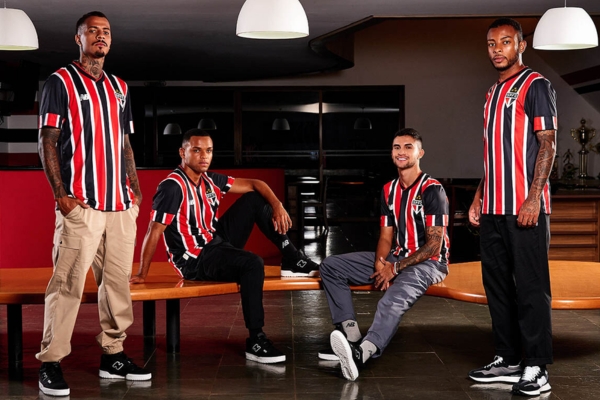 Camisa Reserva São Paulo FC 2024/25 Listrada New Balance - Design listrado vertical em preto, branco e vermelho. Gola V preta com detalhes vermelhos, mangas diferenciadas. Frase dourada "A história começa aqui" na nuca. Escudo Tricolor e logo New Balance no peito. Frase interna "Sentimento que jamais acabará". Selo "Made in Cotia - Atletas e cidadãos" na parte inferior direita.