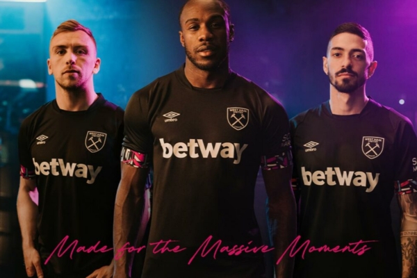 Camisa reserva West Ham Umbro 2022/23 em preto, rosa e azul, inspirada na rampa de lançamento da Thames Ironworks. Escudo Hammers, logo Umbro e detalhes em destaque.