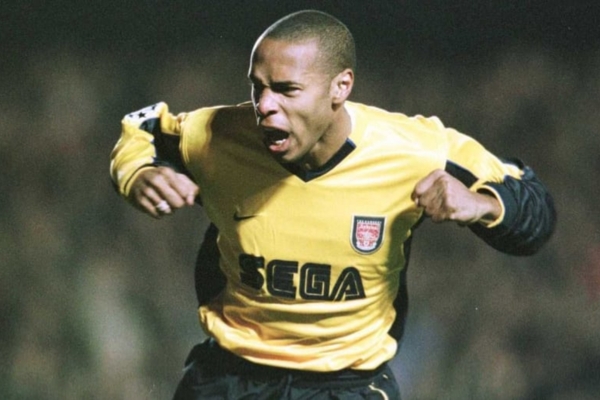 Camisa Retrô Arsenal Nike 1999-2001 SEGA em amarelo e azul, temporada vitoriosa. Thierry Henry, Dennis Bergkamp e Patrick Vieira em destaque. Exclusividade Tevo Sports com 10% de desconto e frete grátis!