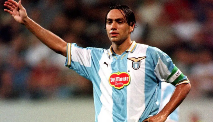 Camisa retrô oficial da Lazio Puma 1999-2000 na cor branca, com detalhes em azul e amarelo. Possui o escudo da Lazio no lado esquerdo do peito e o logotipo da Puma no lado direito. A camisa é branca na parte frontal e nas mangas, com detalhes em azul nas laterais e na gola.