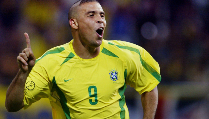 Camisa Retrô Titular Seleção Brasileira Nike 2002-2004. A camisa é amarela e verde, com o escudo da CBF e o logo da Nike no peito. A camisa representa um período de conquistas épicas para o futebol brasileiro, incluindo o pentacampeonato mundial em 2002, a vitória na Copa América de 2004 e o sucesso nas eliminatórias para a Copa do Mundo de 2006.