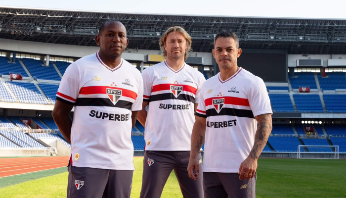 Camisa titular do São Paulo FC 2025, produzida pela New Balance. Modelo branco com gola V em vermelho e preto, escudo centralizado sobre as faixas tricolores e detalhes ondulados inspirados no Morumbi. Edição especial com frase em japonês na gola, selo dourado do tricampeonato mundial e homenagem ao título de 2005.