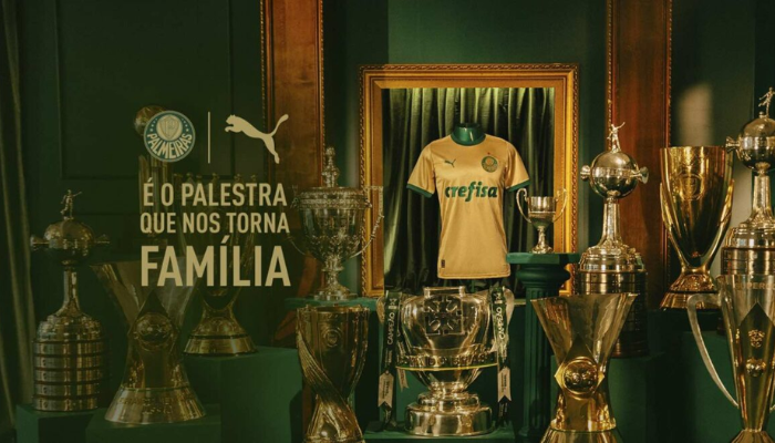 Camisa terceira do Palmeiras 2024-2025 dourada e verde com detalhes em embossing da Cruz de Savóia, símbolo histórico da Casa Real Italiana e utilizado como escudo em 1916. A gola verde escura e a frase “Nasceste Palestra” na nuca complementam o design que celebra as glórias do clube.