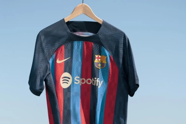 Camisa titular Barcelona Nike 2022/23 em azul e grená, mangas azul marinho, listras verticais em azul royal e vermelho, escudo e Swoosh dourados, estreia da Spotify e ACNUR/ACNUR como patrocinadores máster. Detalhes que celebram a transformação olímpica da cidade.