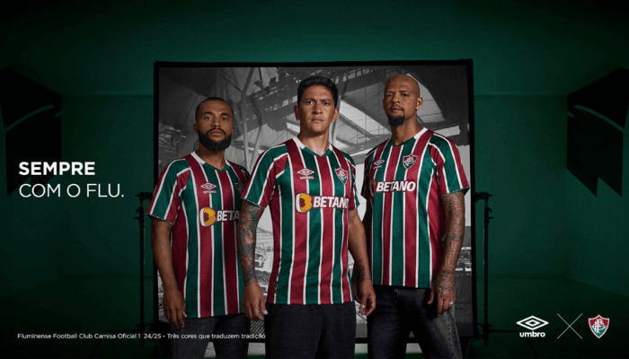 Camisa Titular do Fluminense Umbro 2024-2025. Camisa listrada em verde, branco e grená com gola V, mangas com listras e grafismo em Art Déco, escudo do Fluminense no lado esquerdo do peito, logo da Umbro no lado direito e patrocínio da Betano no centro.