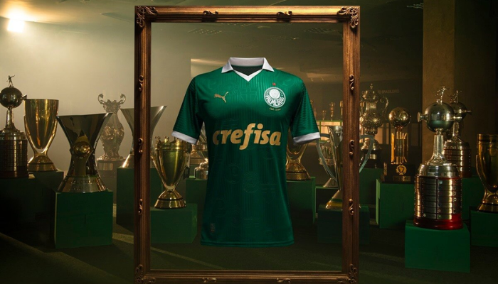 Camisa titular do Palmeiras Puma 2024-2025, com design clássico em verde predominante, gola pólo e punhos brancos, e detalhes dourados. Estampados no corpo estão três escudos históricos do Palmeiras, incluindo o primeiro escudo do Palestra Italia, a Cruz de Savoia e o escudo "P" de 1942.