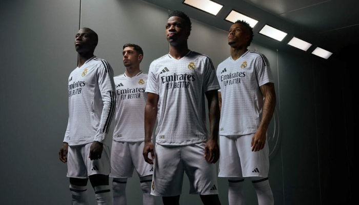 A nova camisa titular do Real Madrid para a temporada 2024-2025 é branca com um padrão houndstooth personalizado com as iniciais RM. As três listras da Adidas nas mangas e os detalhes em preto na gola V complementam o visual. O escudo do Real Madrid está no lado esquerdo do peito, enquanto o novo logo da Adidas aparece no lado direito. O patrocínio da Emirates, Fly Emirates e HP também são estampados na camisa.