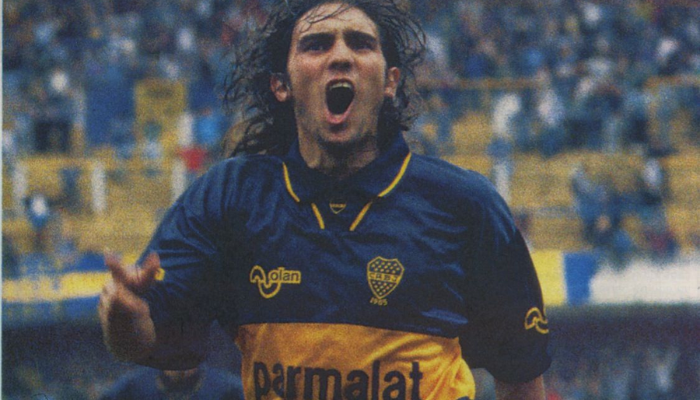 Camisa titular retrô do Boca Juniors 1994-1995. A camisa é azul royal com uma faixa amarela horizontal no peito. O logotipo do Boca Juniors está bordado no lado esquerdo do peito e o logotipo da Olan está bordado no lado direito. A camisa tem gola polo e mangas curtas.