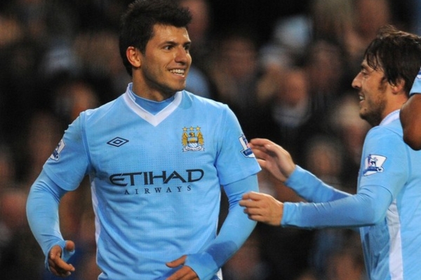 Camisa Titular Retrô Manchester City Umbro 2011/12 em azul celeste e branca, celebrando a conquista épica da Premier League. Destaque para os momentos históricos com gols decisivos de Edin Džeko e Sergio Agüero.