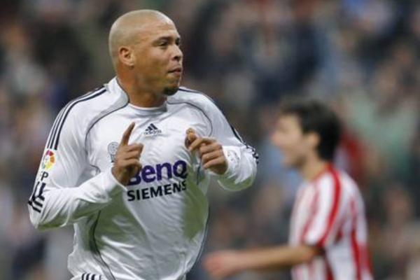 Camisa Titular Retrô Real Madrid 2006-2007 em branco, preto e cinza. Homenagem à conquista da La Liga com Fabio Capello e Ruud van Nistelrooy. Símbolo de paixão e triunfo no futebol.