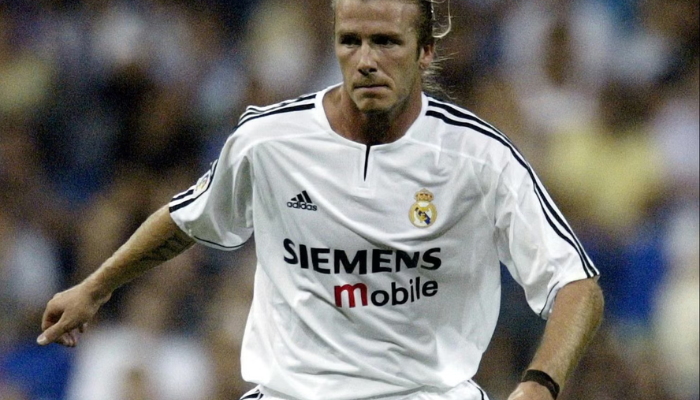 Camisa titular retro do Real Madrid da temporada 2003-2004. A camisa é branca com listras pretas na lateral e detalhes em dourado na gola e nas mangas. O escudo do Real Madrid está bordado no lado esquerdo do peito, e o logo da Adidas está bordado no lado direito. 