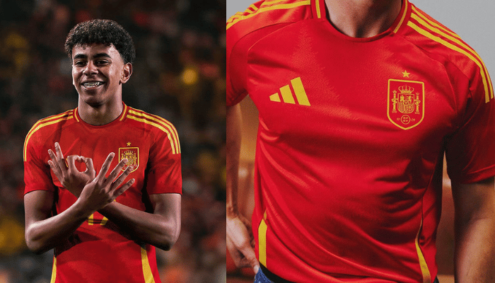 A imagem mostra a camisa titular da Seleção Espanhola para a temporada 2024/25. A camisa é predominantemente vermelha com detalhes em amarelo. Na parte frontal, há um padrão gráfico em ondas em um tom mais escuro de vermelho. Na nuca, há um cravo, a flor nacional da Espanha.