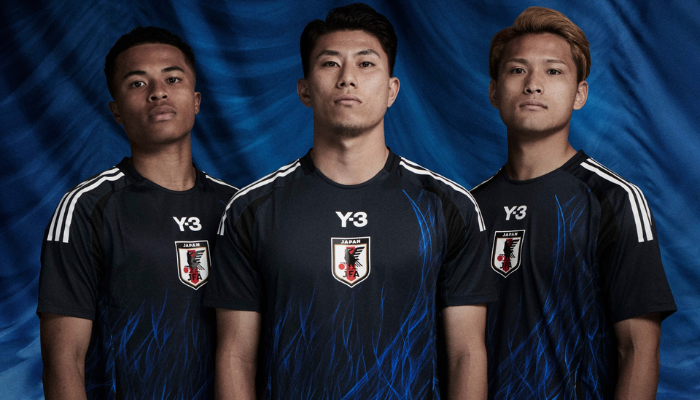 A nova camisa titular da Seleção Japonesa Y-3 2024-2025 é azul marinho e apresenta um gráfico impressionante de chamas azul royal que sobem do corpo do uniforme até o peito. Detalhes em preto adornam a peça, incluindo os arcos laterais e os detalhes triangulares nas axilas, enquanto as icônicas três listras da Adidas percorrem as mangas em branco. 