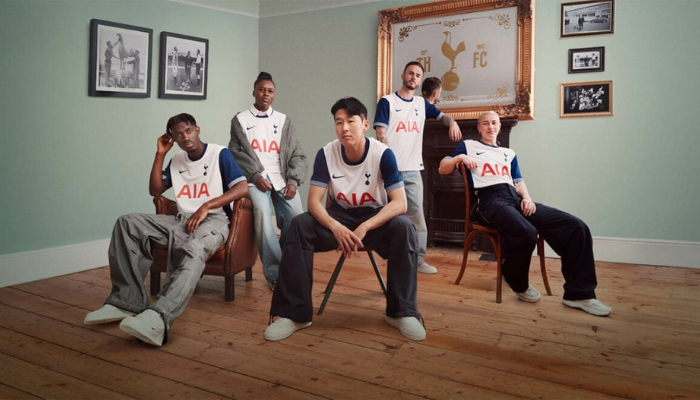 Camisa titular oficial do Tottenham Hotspur para a temporada 2024-2025. A camisa é predominantemente branca com faixas laterais e mangas em azul marinho. A gola é redonda em azul marinho e os punhos trazem um clássico padrão listrado em azul e branco. O escudo do clube está no lado esquerdo do peito, enquanto o logo da Nike está em azul marinho no lado direito