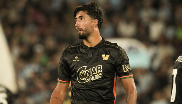 Camisa titular do Venezia FC Nocta 2024-2025, predominantemente preta com gráfico de "Sparkles" em tom sobre tom, gola preta com botão frontal, punhos com detalhes em laranja e verde, laterais do kit em cores complementares, escudo dourado do Venezia no lado esquerdo do peito e logo da Nocta no lado direito.