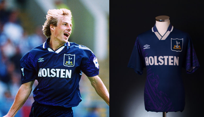 Camisa de futebol retrô do Tottenham Hotspur da temporada 1994-1995, modelo utilizado por Jürgen Klinsmann em sua estreia pelo clube. A camisa apresenta as cores azul marinho, roxo e branco, com o logo da Umbro e o escudo do Tottenham.